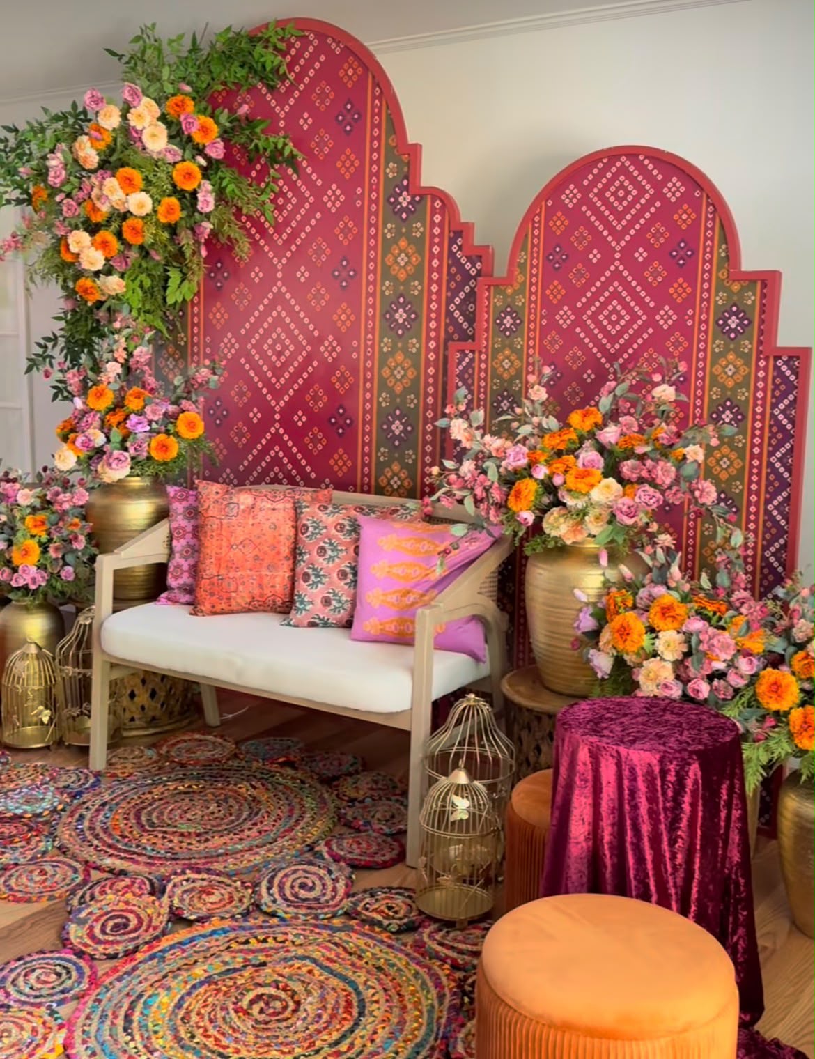 Vibrant pink bandhani arch backdrop with opulent floral arrangements, brass birdcages, and cushioned settee for mehendi