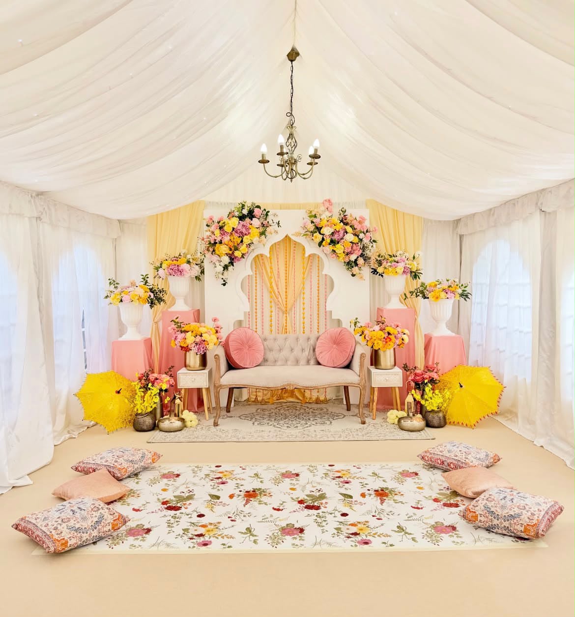 Dreamy white tented mehendi canopy with pastel drapery, floral print rug, and embroidered seating cushions