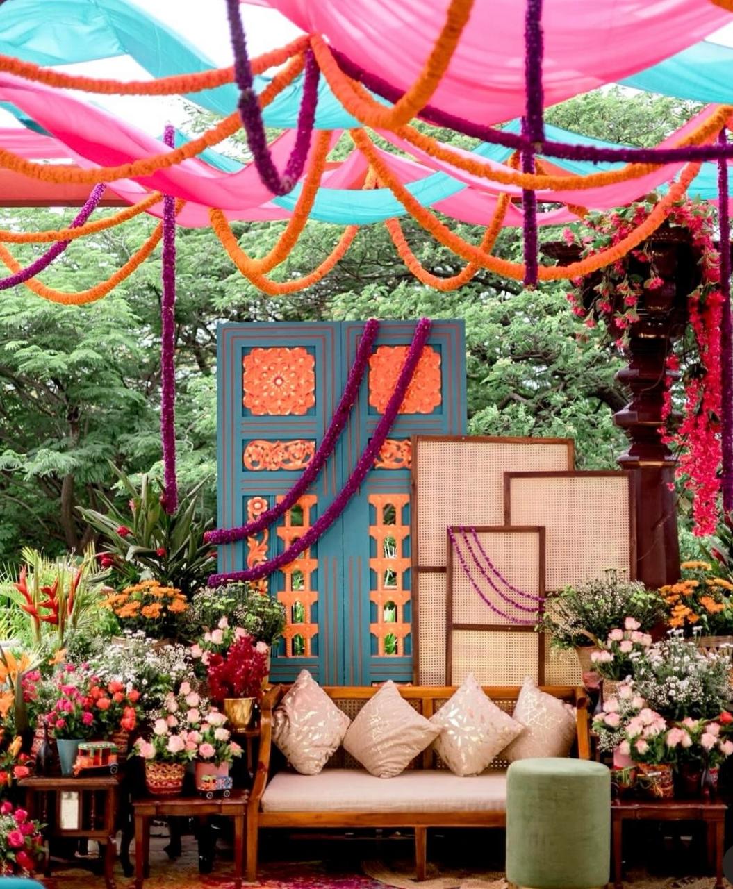 Vibrant outdoor garden mehendi setup with antique blue carved doors, marigold garlands, and rattan screens