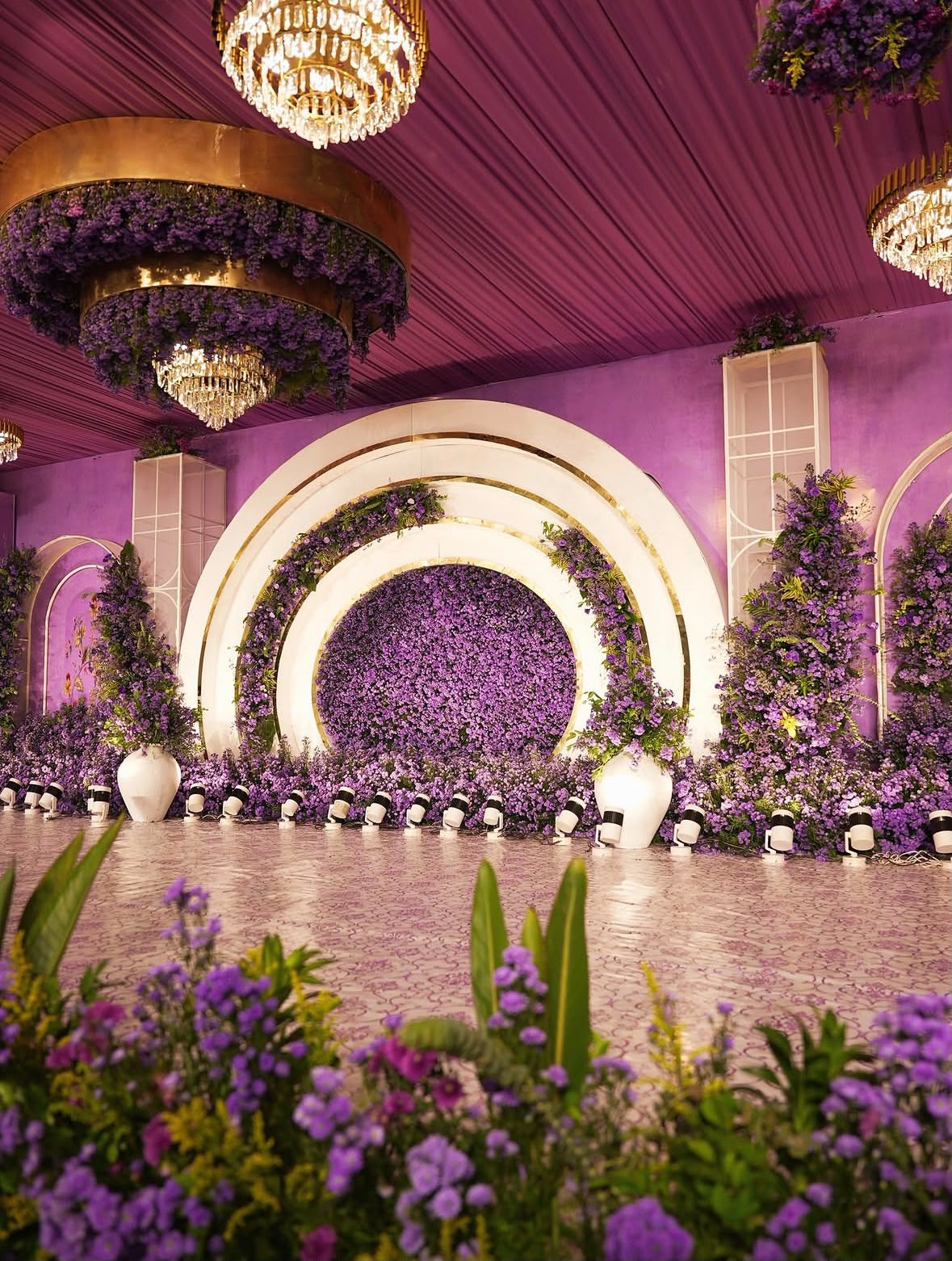 Opulent reception backdrop featuring cascading exotic florals and crystal chandeliers
