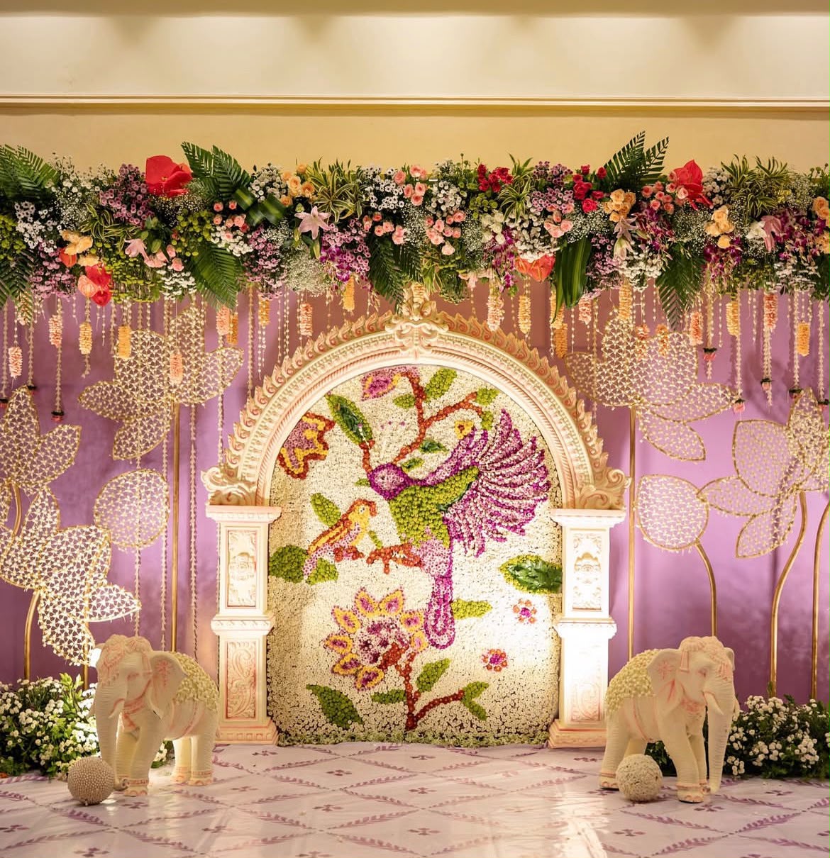 Sacred ceremony stage with Lord Krishna painting, wooden pillar arch, and fragrant flower strings