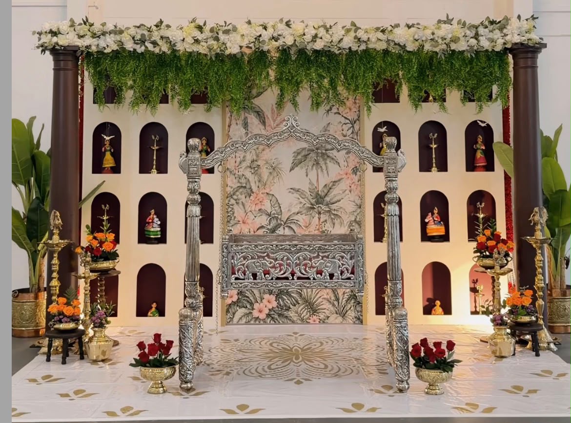 Ornate festive stage with vintage carved settee, flower baskets, and ceremonial offerings